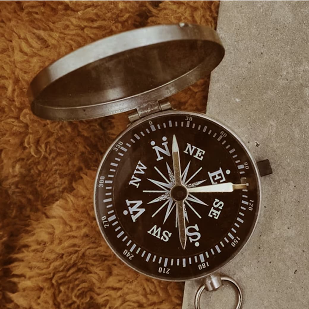 Vintage silver Optimize logo compass with black dial and white markings, resting on a textured surface.