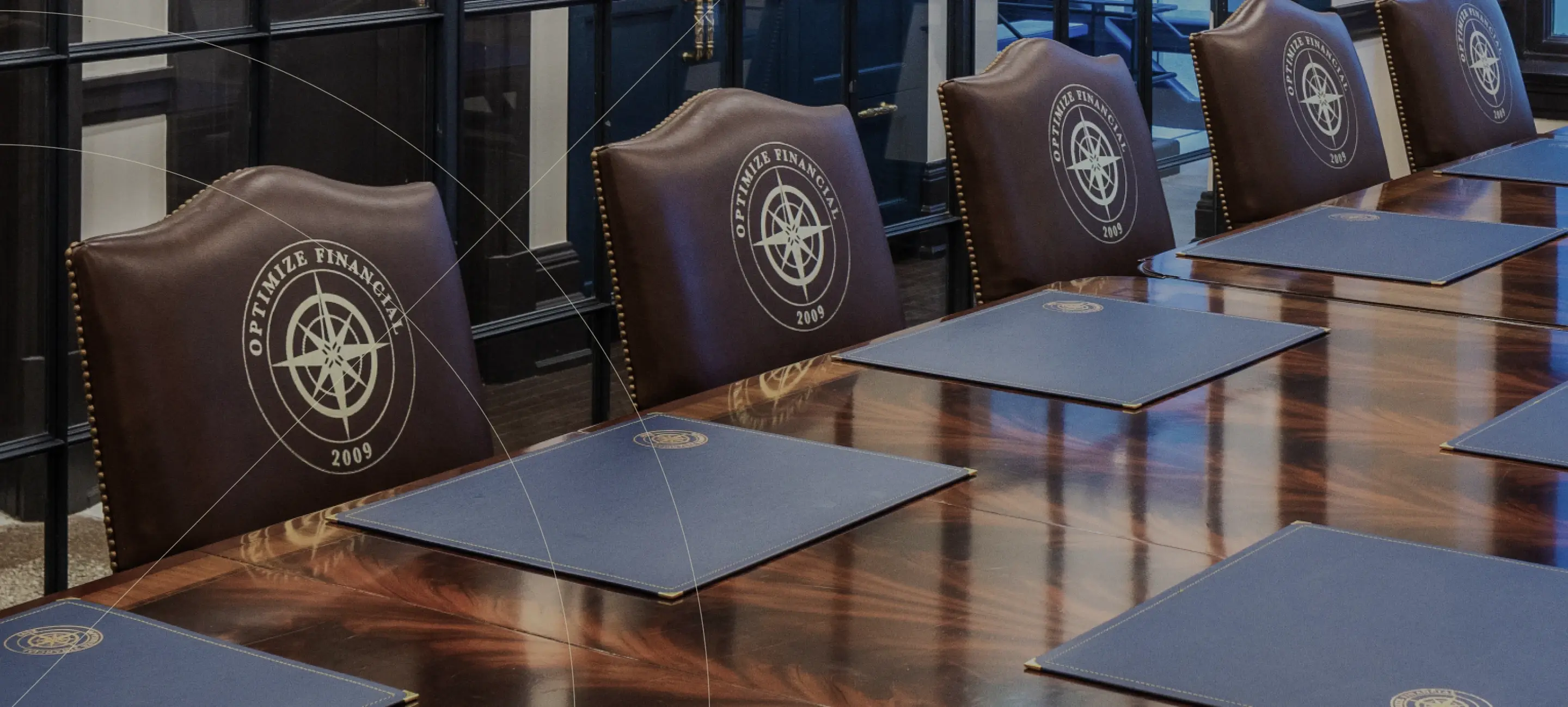 Row of brown leather chairs with logos on the backrests, arranged behind tables in a formal meeting room.