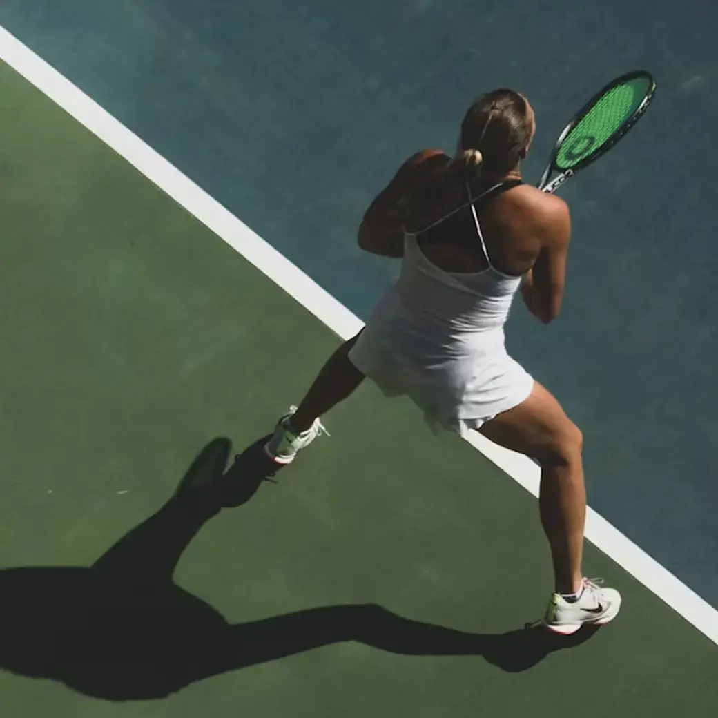A person in a white outfit on a tennis court, preparing to hit the ball with a racket.