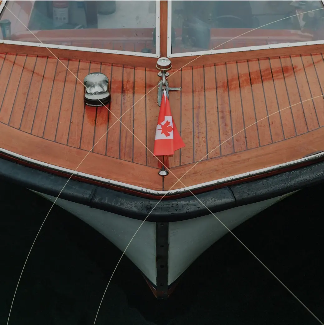 Close-up of a wooden boat deck with a small Canadian flag at the bow, docked on dark water.