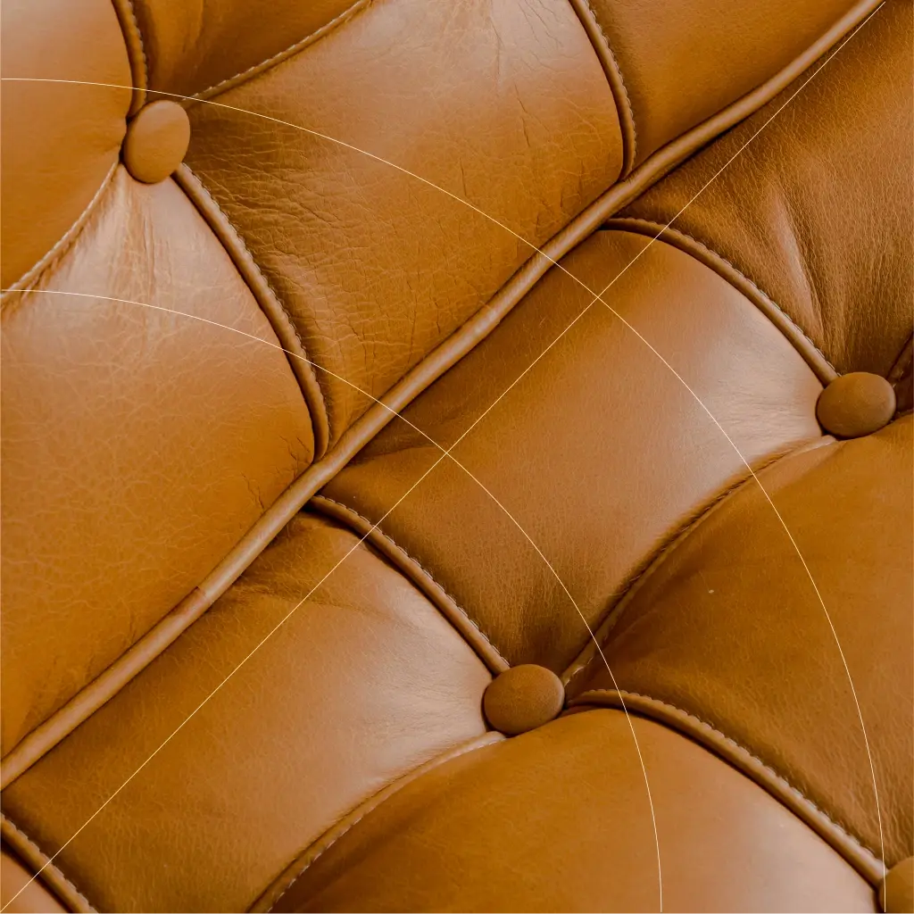 Close-up of brown leather upholstery with button-tufted stitching, showing texture, seams, and natural creases in the material.
