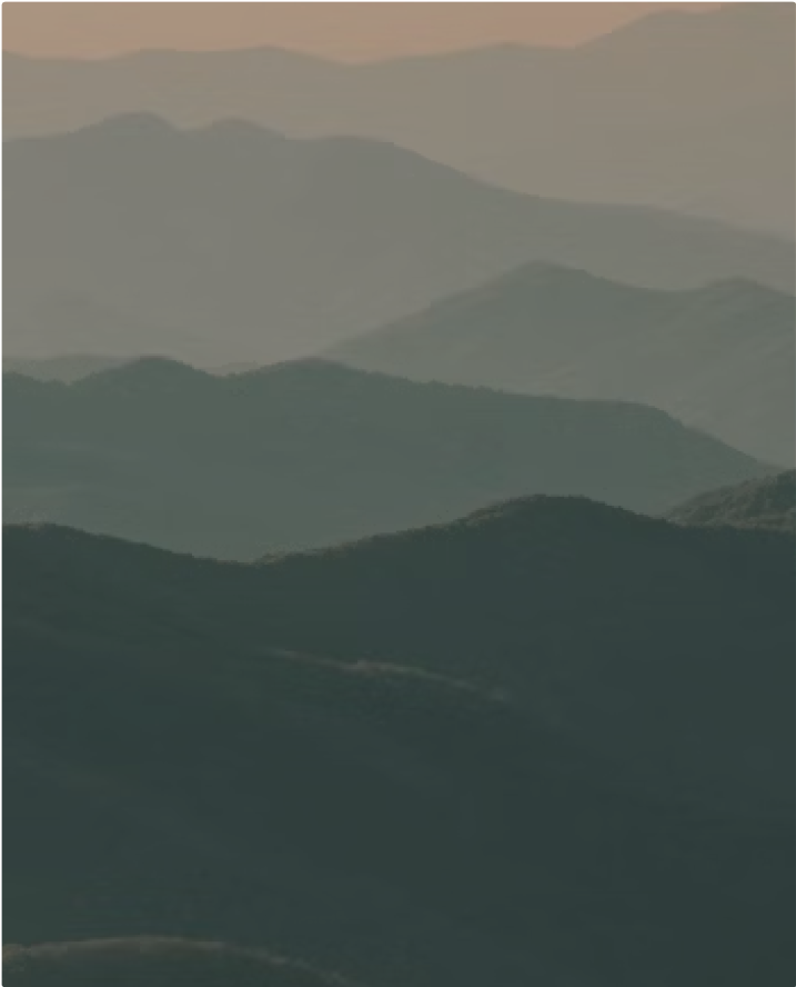 Layers of rolling mountains fading into the distance under a hazy, peach-colored sky, creating a serene and atmospheric landscape.