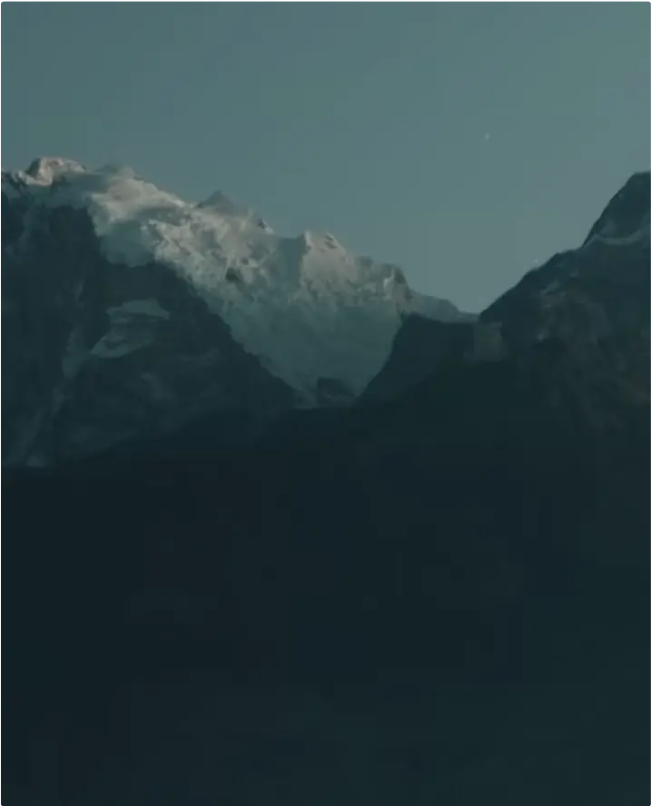 Snow-capped mountain peaks rising above dark shadowed ridges, set against a clear blue sky.