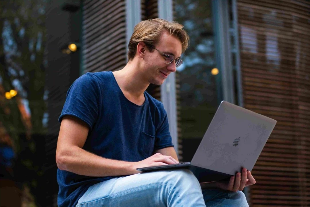 Blonde Millennial with blue t-shirt with a mac book 